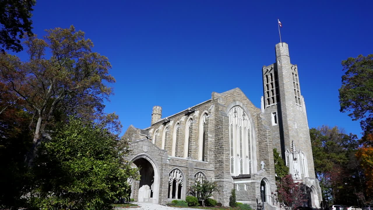 Gothic church with bell tower surrounded by trees on clear, blue sky day.