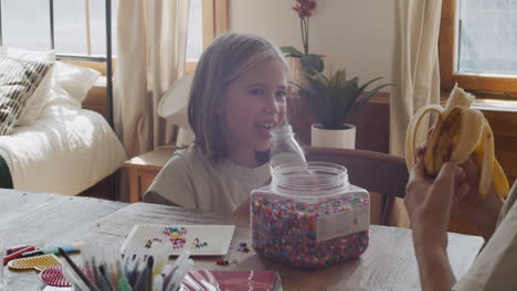 a pretty blonde little girl drinks water while her happy mother holds a banana