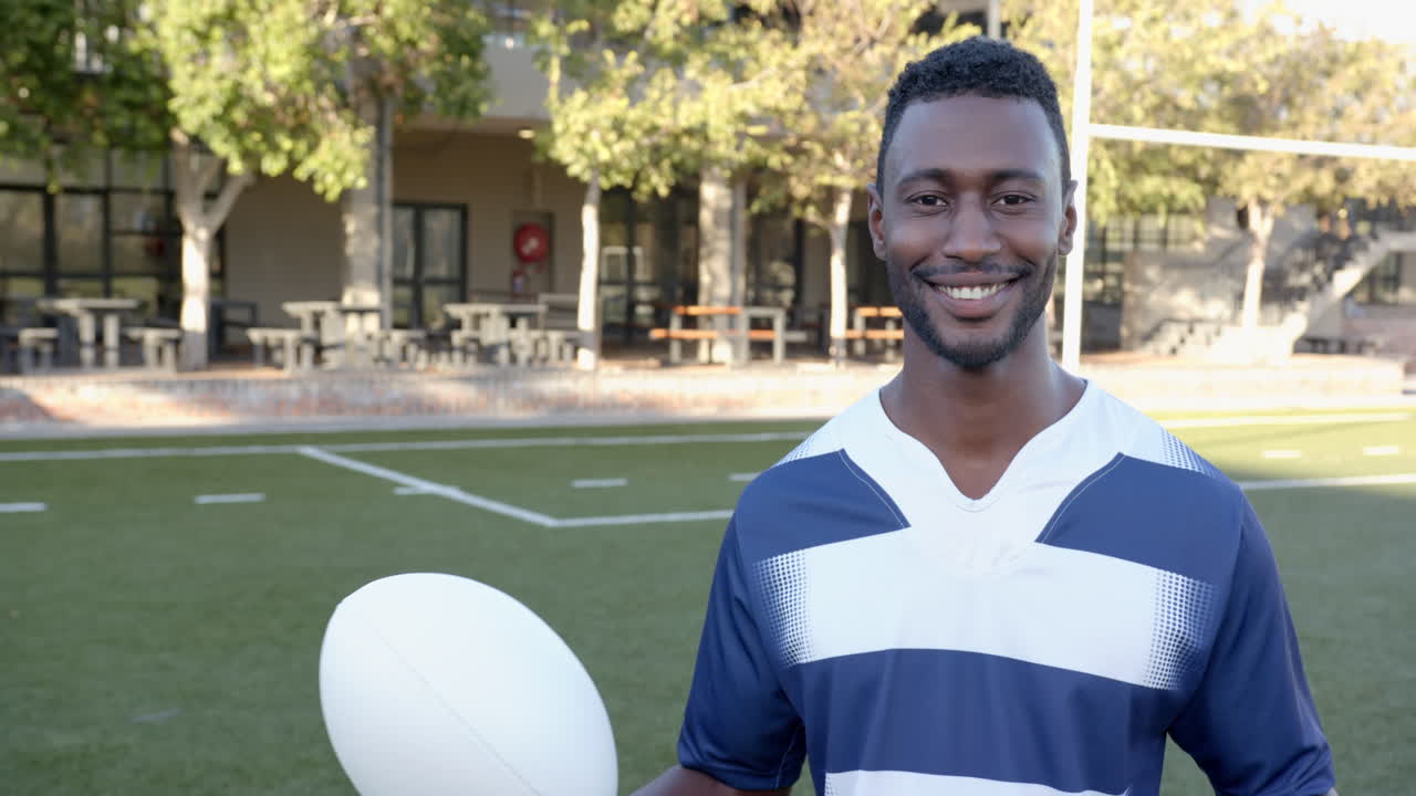 Atleta masculino afro-americano sorrindo com camisa esportiva de pé em campo, com espaço para texto