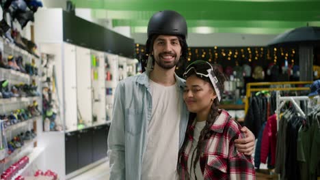 Portrait-of-smiling-couple-posing-in-helmet-and-ski-glasses-during-shopping-in-sport-goods-store