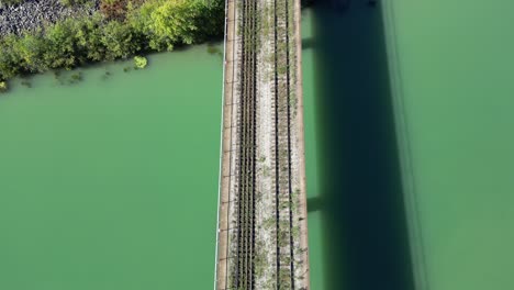 vía férrea abandonada sin fin en el puente sobre el río que se dirige al bosque, antena