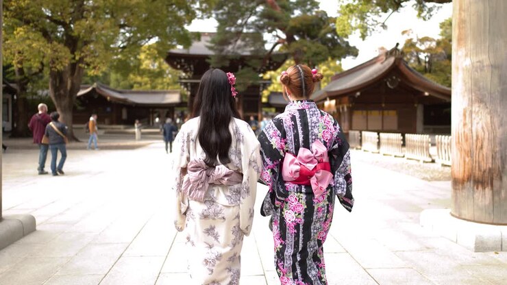 Vista da dietro di due donne che indossano kimono floreali mentre camminano attraverso un torii di legno