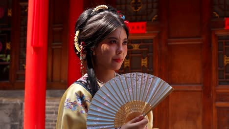 mujer sonriente de qing con ventilador en el patio tradicional chino usando un ventilador de mano contra el clima caluroso