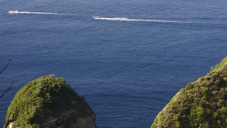 Tourist-boats-sail-on-the-waters-around-Kelingking-Beach,-Nusa-Penida,-Bali,-Indonesia