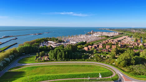 footage over the greenery approaching large yacht club in lelystad, the netherlands. vast waterscape of the markermeer lake with dams at backdrop.