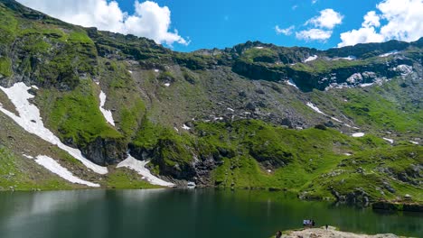 Espectacular-Lapso-De-Tiempo-Del-Lago-Balea-Una-Vista-Cautivadora-De-Los-Picos-De-Las-Montañas-Nevadas,-La-Hierba-Verde-Y-El-Cielo-Azul-Claro-Con-Nubes-Blancas-Que-Se-Mueven-Rápidamente-En-El-Transfagarasan-De-Transilvania,-Rumania