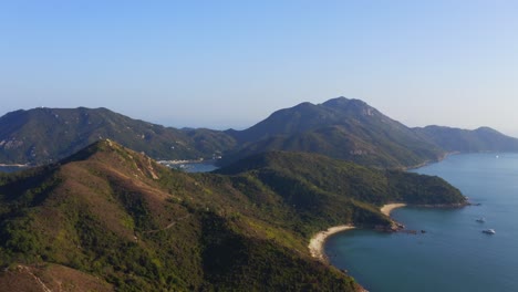 cinematic drone shot traveling forward and upward of the coast of an island with some beach to reveal a fisher village behind the mountains