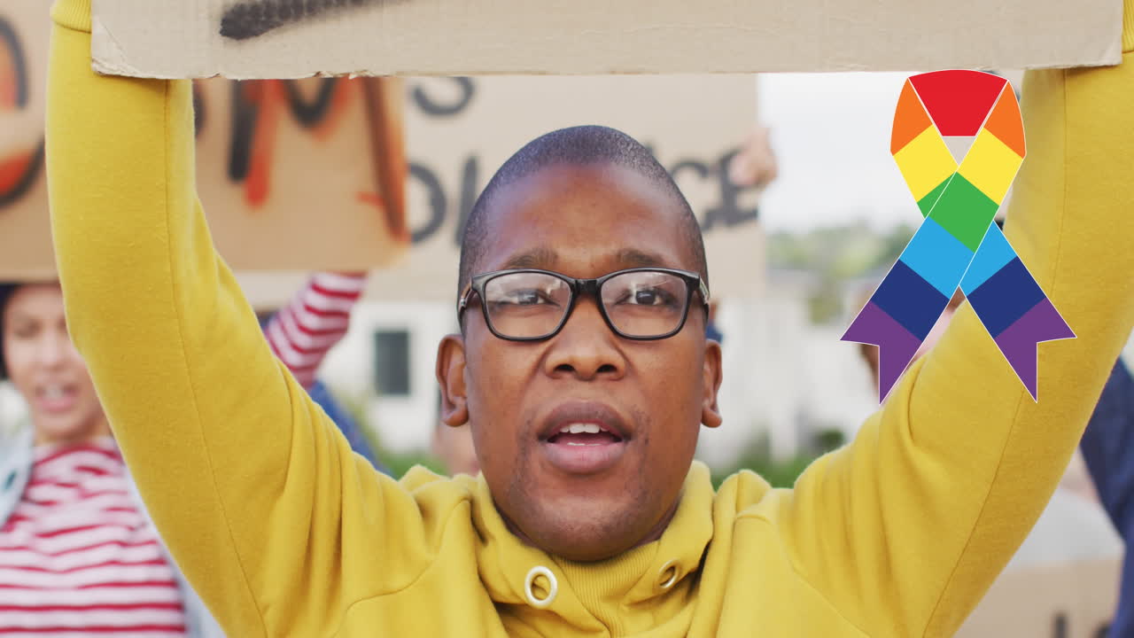 Animation of rainbow ribbon over african american male protester with banner