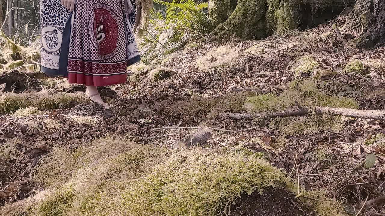 Woman shaman walking left to right barefoot through lush moss covered rainforest honoring her ancestors