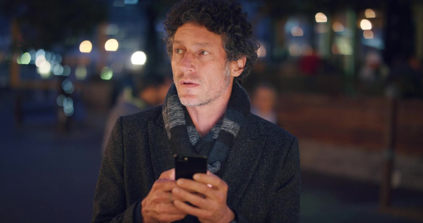 Middelaldrende mann som bruker smarttelefon på gate i byen om natten