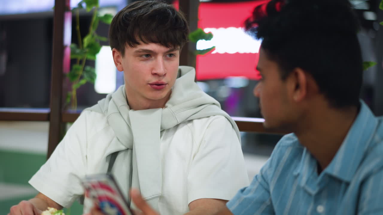 Teenager wearing white shirt nodding in agreement to video while friend explains content, indoor casual setting, close shot of facial expression and hand gesture showing understanding and engagement