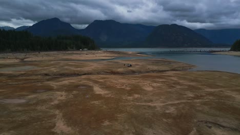 aerial of black truck people nearby starts high angle swiftly approaching truck against mountains and lake dark moody scene intense clouds hinting at storm pans down as drone nears