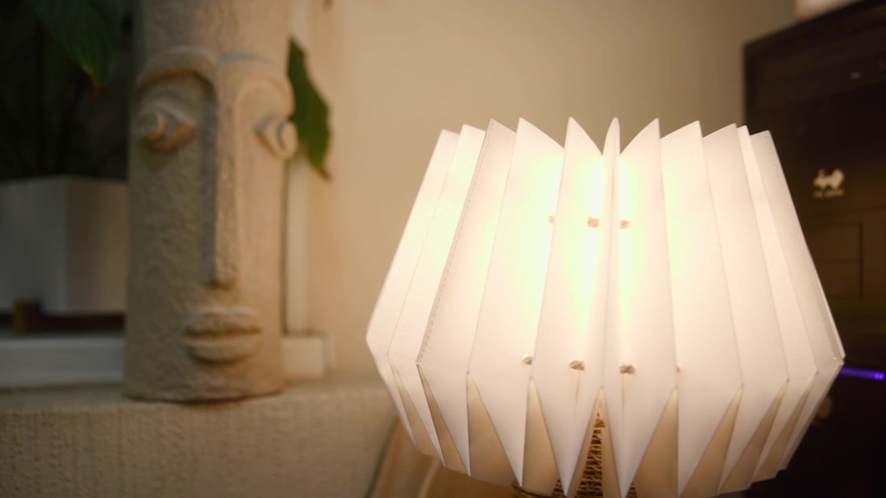 Lámpara de origami luminosa junto a una escultura con pantalla de papel plisado que se despliega para emitir una cálida luz ambiental. Medios