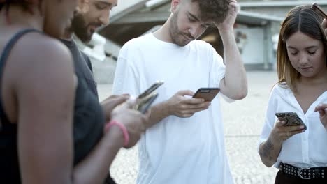 Serious-friends-standing-in-circle-on-square-with-phones