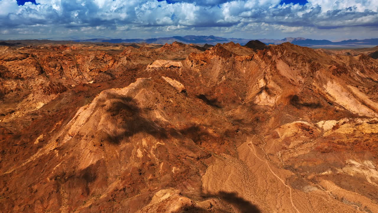 Shadows from the clouds slowly move by the tops of brown rocks. Arid lifeless mountainous landscape of Mojave desert from aerial view.