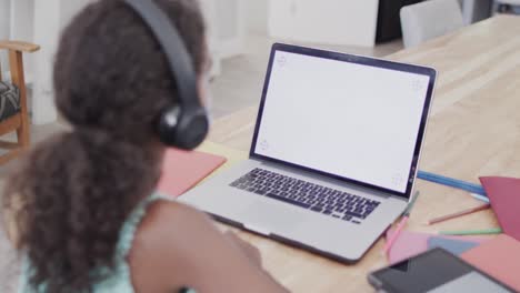 Chica-Afroamericana-Sentada-En-La-Mesa,-Usando-Una-Computadora-Portátil-Con-Espacio-Para-Copiar-Lecciones-En-Línea,-Cámara-Lenta