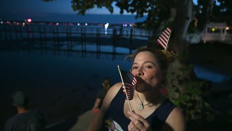 woman wearing american flags and kissing the us flag at night during july 4th celebration