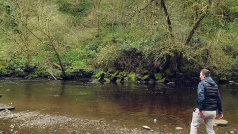 Hand-held-shot-of-a-young-man-skipping-stones-on-a-calm-river-in-summer