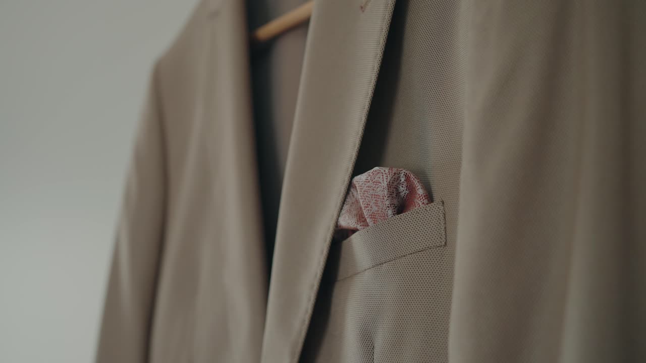 Primo piano di una giacca da abito beige con un fazzoletto da taschino a fantasia piegato nella tasca.