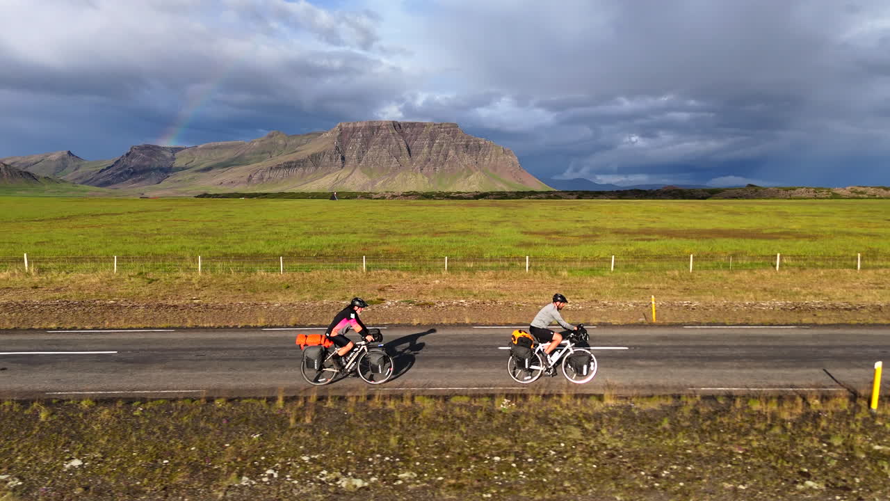 スナイフェルスネス半島を探索：虹と山を背景に54号線を走る2人のサイクリスト