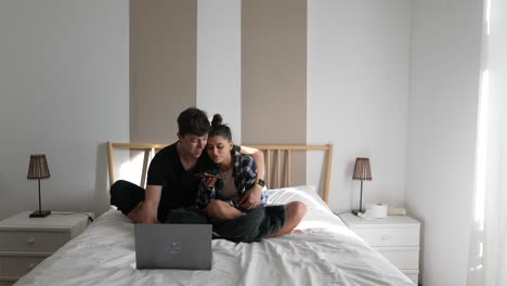 pareja relajándose en la cama, usando el portátil y el teléfono