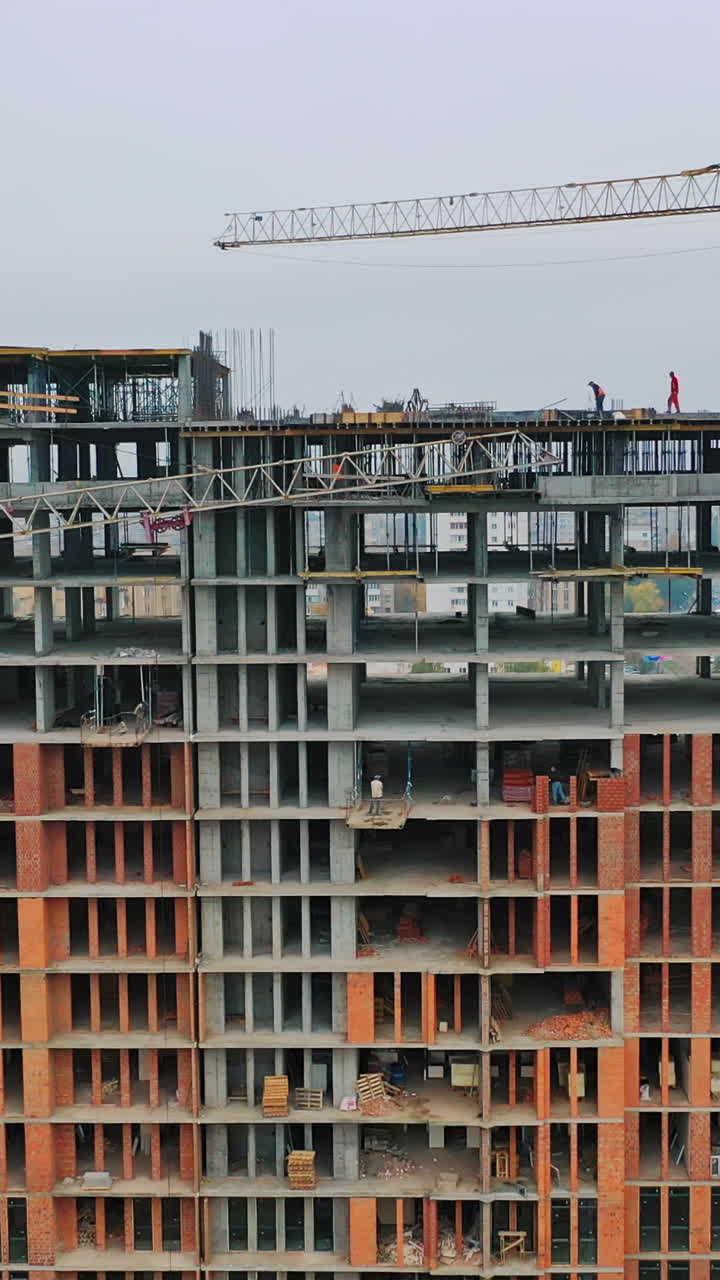 View of building at construction site. Aerial flight over new constructions site development where heavy machinery and construction workers are working with power tools