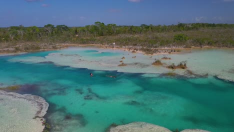 people jumping into tropical rapids of bacalar in mexico, aerial view