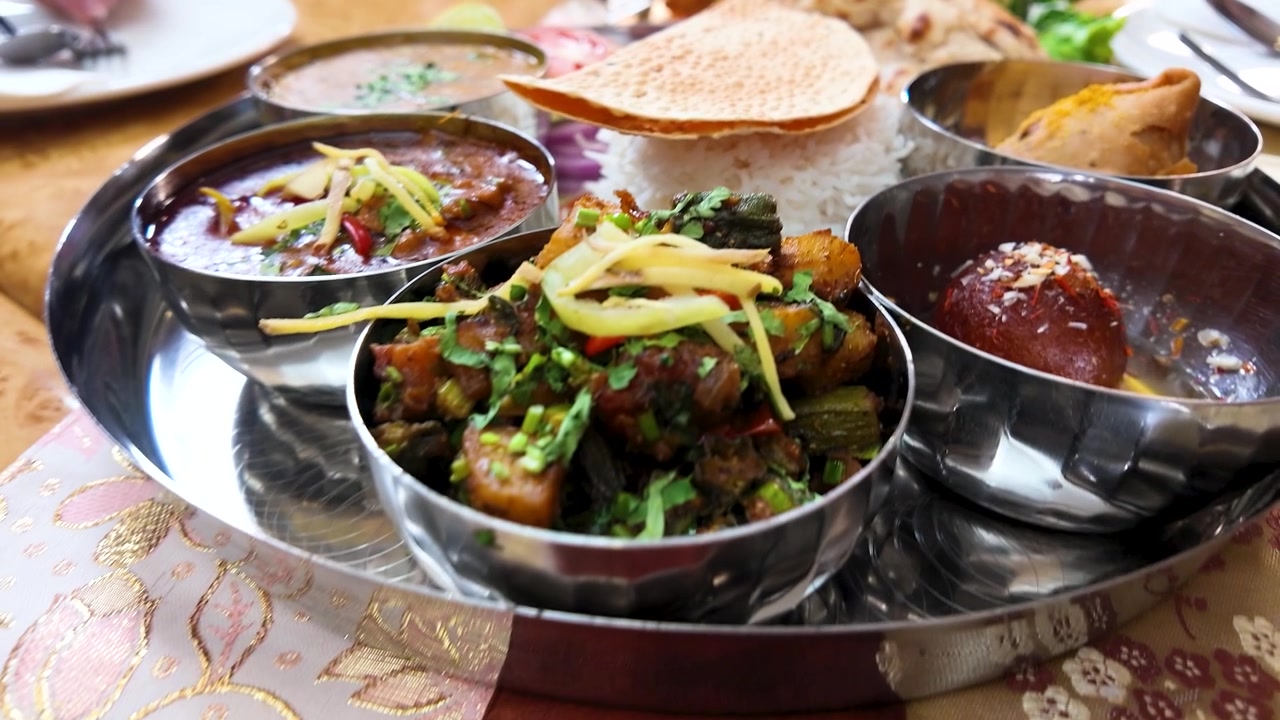 Pengambilan gambar panning jarak dekat hidangan tradisional India termasuk naan, samosa, dan kari di Bangkok.