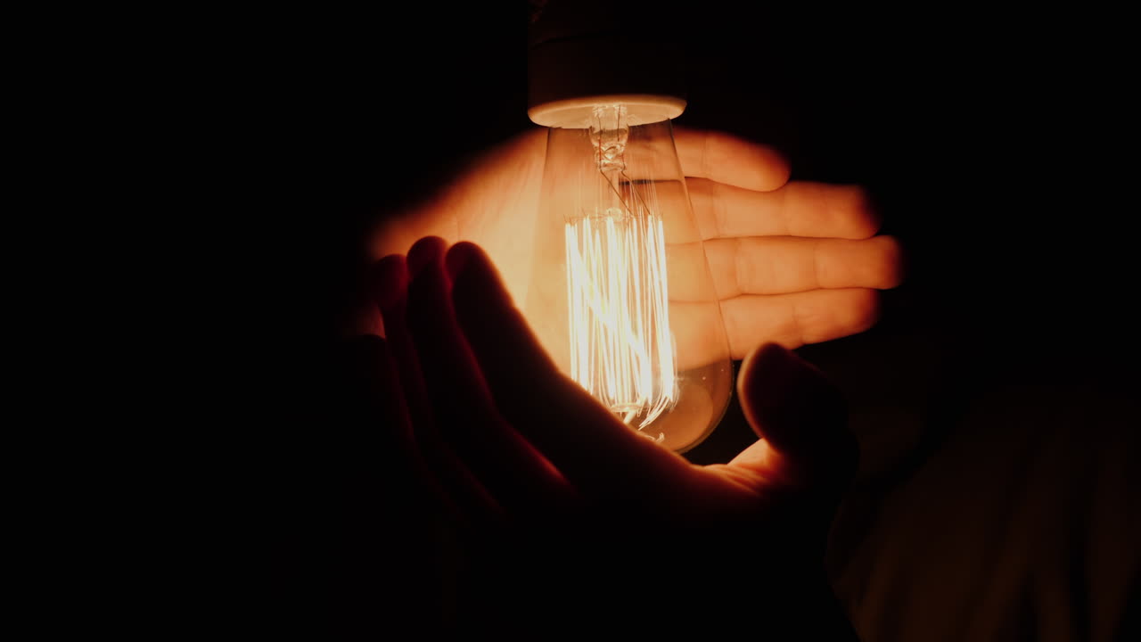 A Man Holds His Hands Around An Electric Light Bulb