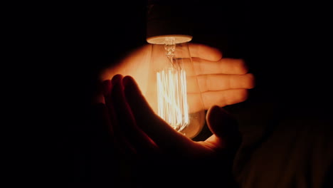 a man holds his hands around an electric light bulb