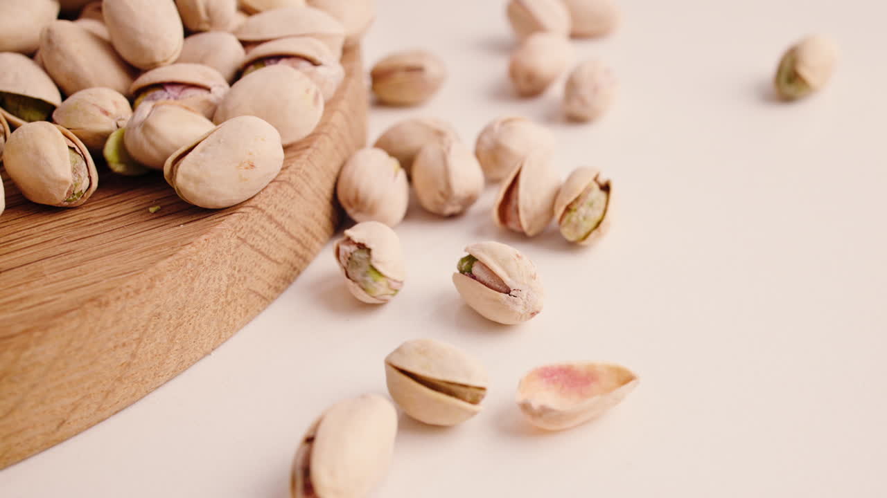 Pistacchi che cadono e si spargono su una superficie bianca con una tavola di legno