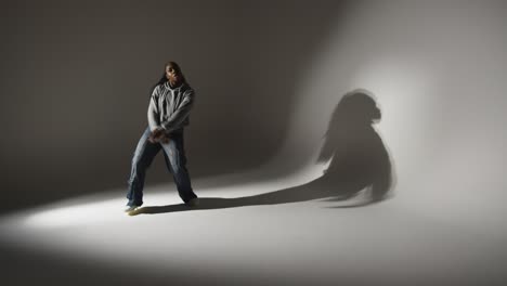 retrato de estudio de larga duración de una mujer joven bailando proyectando sombras con iluminación baja contra un fondo gris 3
