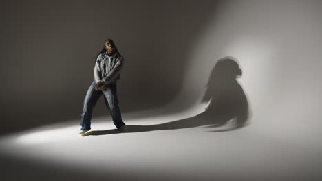 full length studio portrait shot of young woman dancing casting shadow with low key lighting against grey background 3