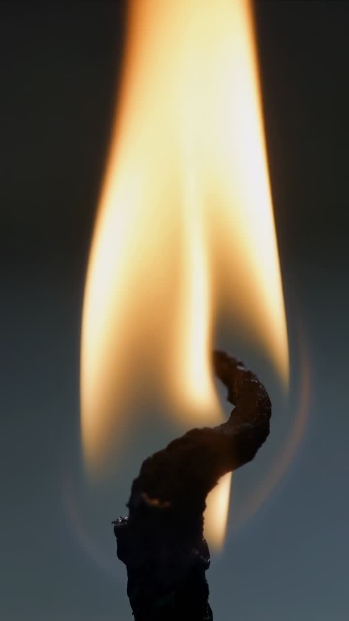 Vertical video: Flickering candle flame pulsing above burnt wick in drafty room with wax base
