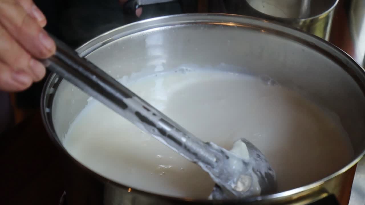 Person preparing homemade cheese, stirring curdled milk in a pot as steam rises, capturing a warm and traditional kitchen moment