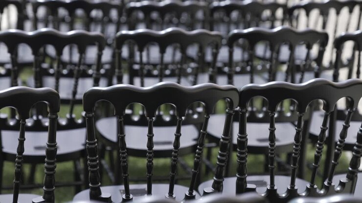 No audience yet - Multiple black chairs arranged in rows for an event, ceremony or wedding with a focus on their glossy, ornate backs.