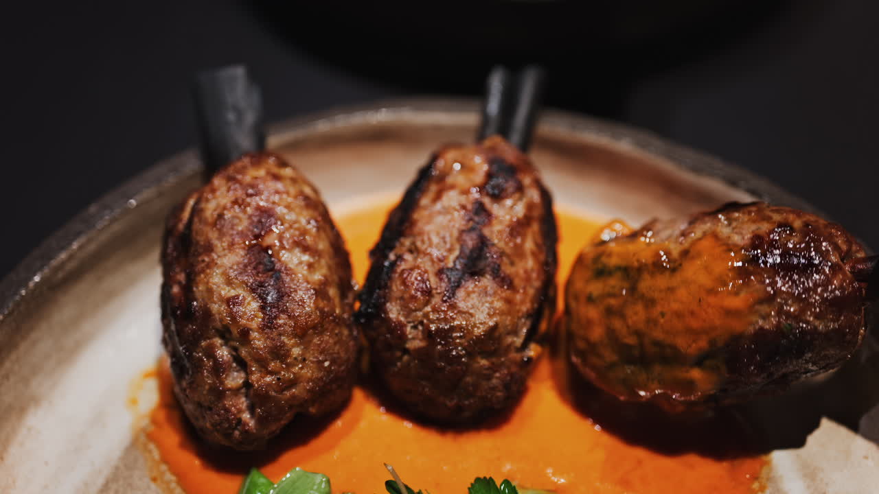 Three grilled meat skewers on charcoal sticks served on a plate with an orange sauce