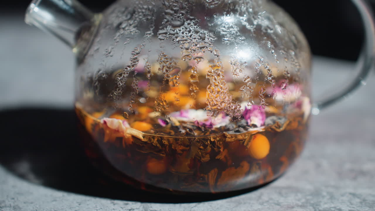 Sunlit Glass Kettle With Herbs, Herbal Infusion In Clear Glass Teapot With Decorative Accents, Sunshine Illuminated Glass Teapot Steeping Fragrant Herbal Tea Amidst Artisanal Surroundings