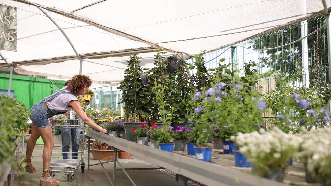Gardener showing plants to young customer in greenhouse