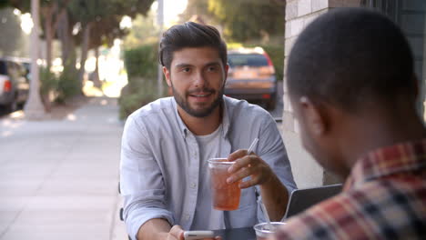 two adult male friends talking over cold drinks outside cafe