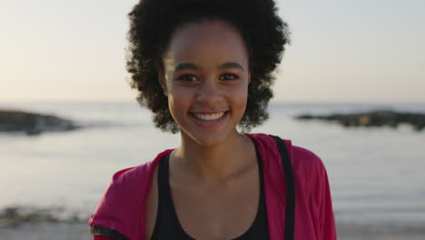 Porträt-Einer-Jungen-Afroamerikanischen-Frau-Am-Strand,-Die-Verspielt-Lacht-Und-Eine-Rosa-Jacke-Trägt