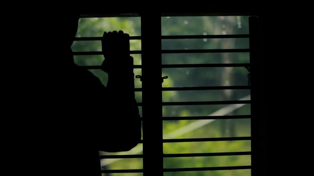 Silhouette of unrecognizable bored person watching rain through window. Static