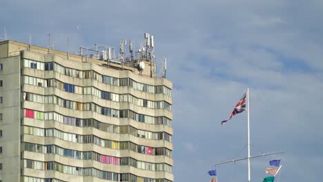 bandera del reino unido junto a un bloque de pisos con ventanas coloridas y satélites en la parte superior del edificio en cámara lenta de día soleado