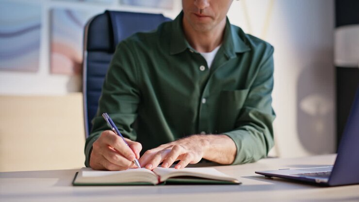 HR manager talking video meeting making notes in notebook at desk closeup
