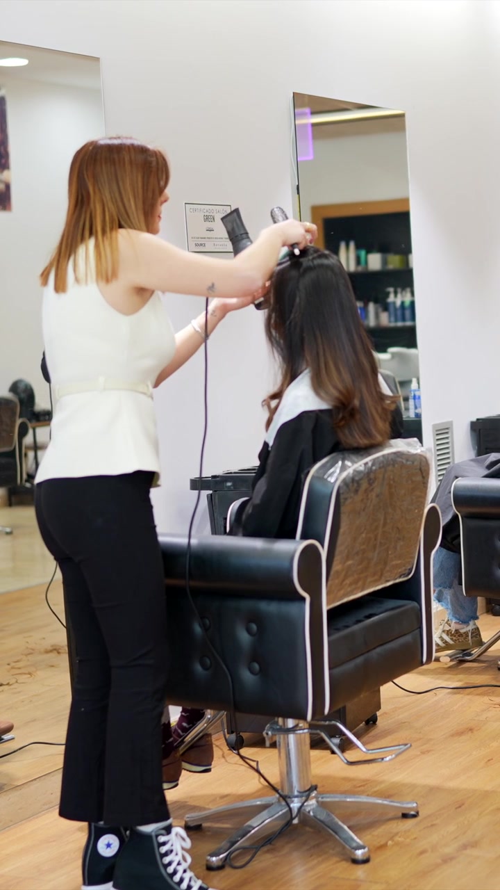 Parrucchiere che asciuga i capelli di una cliente in un salone professionale