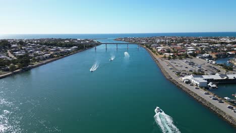 aerial of boats in channel of water and cars driving over bridge in background