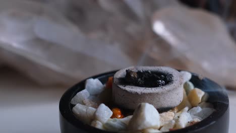 close up shot of burning incense with white smoke in a bowl with quartz crystal gemstones in the background, in 4k slow motion