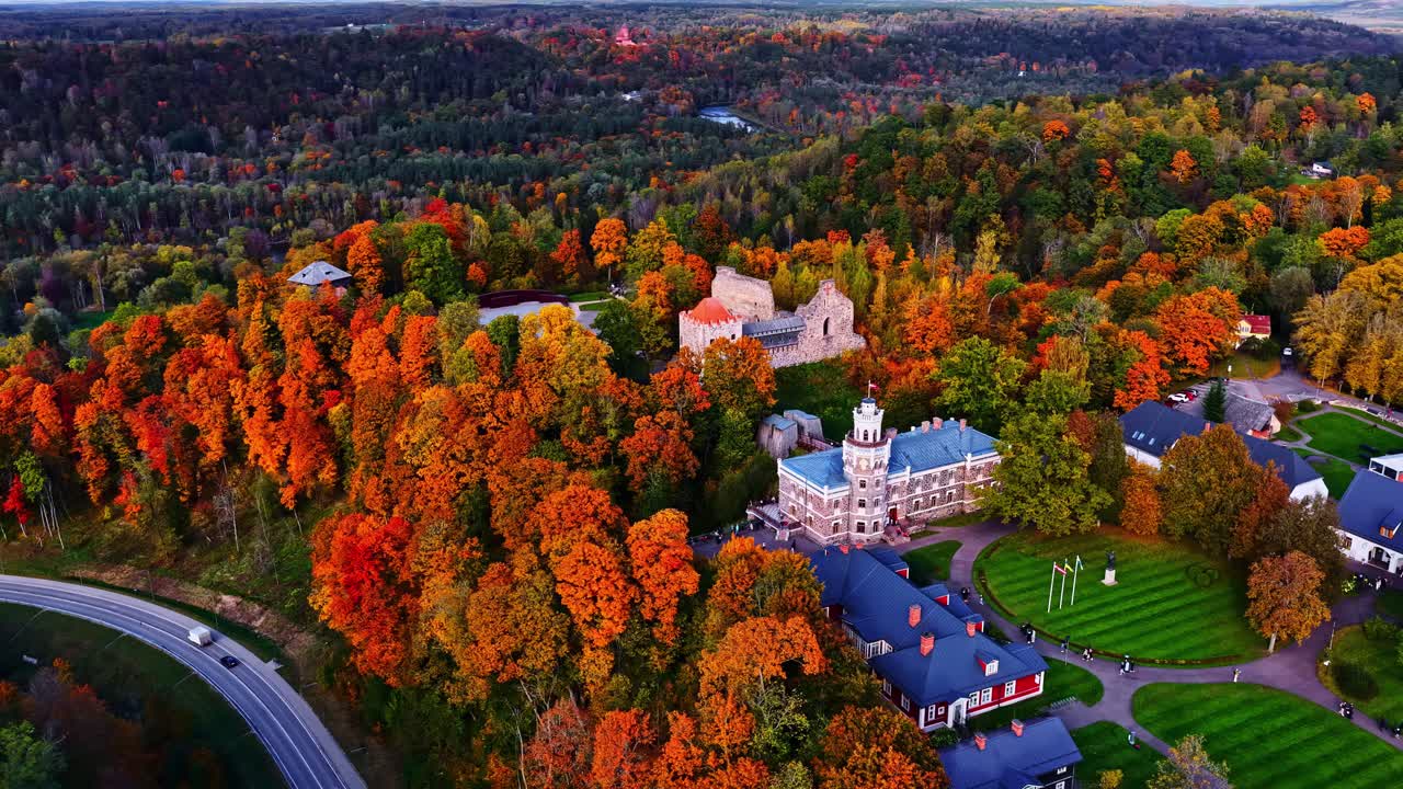 Aerial establishing pan of castle grounds, autumn forest and houses under bright sunlight