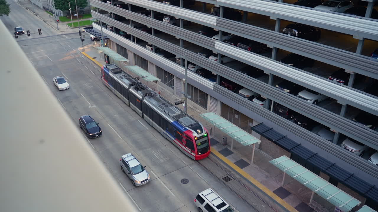 Gündüz saatlerinde Houston şehir merkezindeki bir otoparkın ve şehir trafiğinin yanından geçen Houston METRORail hafif raylı treni, Houston, Teksas, ABD'deki toplu taşıma altyapısını sergiliyor.