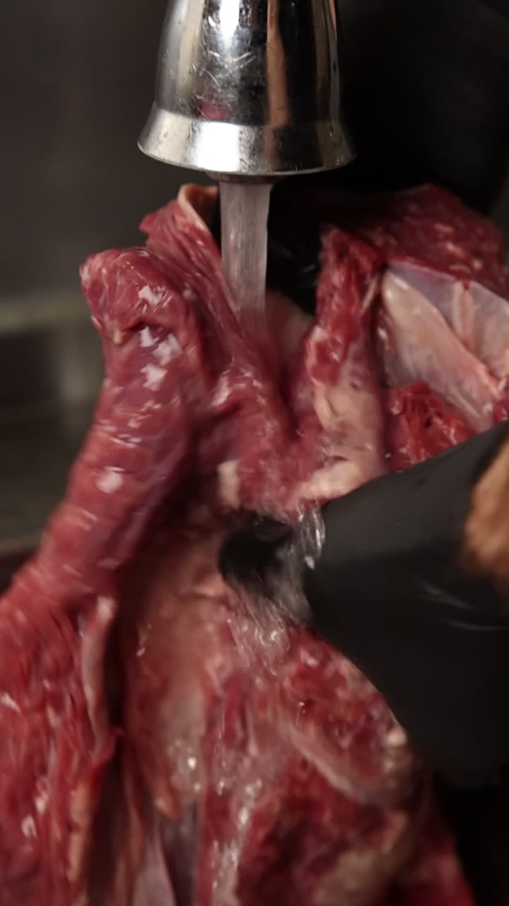 Persona con guanto nero che lava carne cruda sotto l'acqua corrente